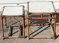 Two vintage rattan and bamboo nesting side tables with white tops shown side by side for scale and style.
