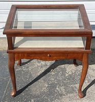 Front view of wooden side table with glass top and drawer, showing cabriole legs and pull-out drawer.