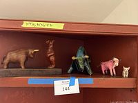 Shelf with five figurines: wooden bull and bear on base, abstract glazed bison, pink cow, cream cat