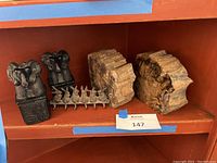Photo showing goat head bookends, Egyptian carving bookends, two pieces of petrified wood, and a bunny key hook on a wooden shelf.