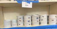 Wide angle photo showing multiple stacked white soufflé bowls with butterfly and blueberry designs, and solid white bowls on shelf