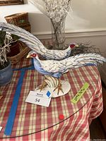 Pair of blue and white ceramic pheasants with detailed feathering, posed on an oval base, shown on a plaid tablecloth.