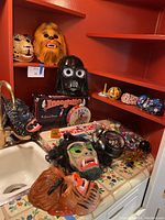 Photo showing six plastic masks including cheetah, furry creature, Darth Vader, green-faced werewolf, wolf/dog, gorilla masks plus classic games and noise makers on shelf and counter