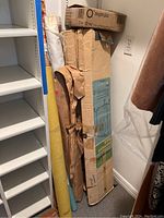 Fabric rolls, boxed metal clothing rack, and Better Oxygen Plus can box stacked upright in corner of room