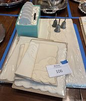 Photo showing folded embroidered linen napkins and tablecloth with small silver bells on top, arranged on a wood surface.