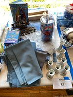 Overview photo showing blue linen napkins, brass menorah, Chanukah candles in packaging, and white bud vase place card holders arranged on tablecloths