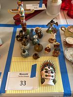 Overview photo showing the collection of miniature vases, Native American themed figurines, totem, and mask on a white surface with blue tape sections.