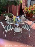 Full patio set with round glass table, four wrought iron chairs with cushions, and umbrella in outdoor setting