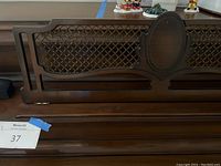 Close-up of piano decorative lattice panel with oval central medallion on dark wood.