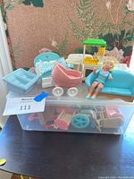 Overview of lot showing blue bed, blue cradle, pink bathtub, blue couch, green canopy stove, white sink, small table with placemats, and doll figure seated on couch.