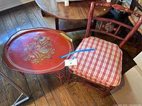 Side chair with carved lacquer finish and red plaid cushion alongside low red lacquer tin tray table with floral decoration on tray