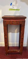 Full view of the small red Asian side table showing overall shape, height, and red paint with decorative inlay patterns.