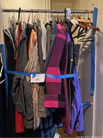 Rack of vintage men and women clothing tightly packed, featuring coats and jackets of various colors and materials including a pink and purple striped knit jacket, fleece outerwear, and a black leather jacket.