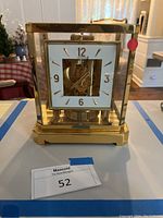 Front view of gold-tone cube clock showing white dial, gold numerals and visible internal movement