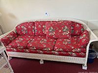 Full view of white wicker couch with red floral cushions in a living room setting.