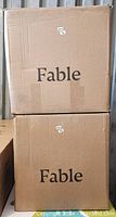 Two sealed cardboard boxes with 'Fable' brand labeling, containing the two dining chairs