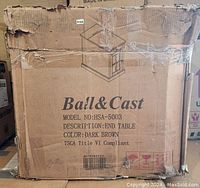 Photo of cardboard box packaging showing the brand Ball & Cast, model HSA-5003, description as End Table, color dark brown, with visible shipping damage on the box edges.