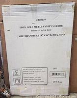 Photo of the original packaging box labeled 'Eden, Gold Metal Vanity Mirror' with size 24x36 inches and care instructions.