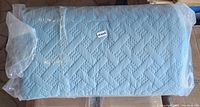 Photo of the rolled and wrapped full/queen size comforter, light blue with quilted geometric pattern.
