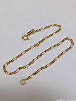 Single delicate 14K gold bracelet laid flat on white surface showing chain details and clasp.