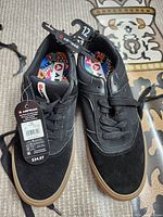 Photo of black Airwalk men's shoes in size 12 with original tags showing price and size, placed on a patterned surface.