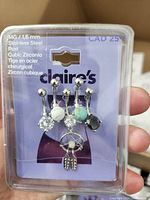 Photo showing 4 belly button rings in original Claire's packaging with clear plastic cover. Rings include cubic zirconia stones and a dreamcatcher charm.