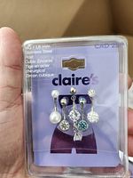 Clear image showing the full set of five silver tone stainless steel belly button rings by Claire's on retail backing card. Each ring features cubic zirconia or pearl decorative elements in various shapes and colors.