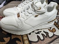 Side view close-up of the white leather sneaker showing gold accents on heel and sides.