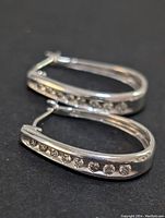 Close-up of a pair of sterling silver hoop earrings with a row of lab-created diamonds on each, showing polished metal and clear stones.
