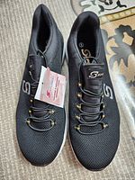 Top view of a pair of black women's sport Skechers shoes, size 9, with mesh fabric, laces and tags attached.