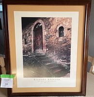 Photo of framed wall art showing a rustic stone building door with arch and steps, brown frame