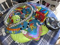 Photo showing the colorful children's play mat with animal prints, VTech activity toy, black and white gym arch, green plush caterpillar, and collapsible play tunnel.