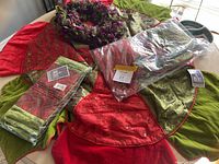 Top view displaying multiple Christmas tree skirts and table runners in red and green with floral embroidery, some items still in packaging.