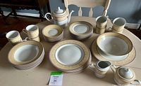 Photo showing all dishes arranged on a table; includes plates, bowls, mugs, teapot, creamer, sugar bowl with matching beige/gold pattern.