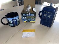 Two Doctor Who-themed mugs displayed with the smaller mug's original box between them on a white table.