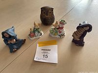 Photo showing five figurines: brown owl, two snowmen with green scarves, blue-hooded figure sitting, purple-hooded figure playing accordion, photographed on a light surface with a label.