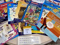Close-up photo showing a variety of educational workbooks including handwriting, phonics, math, and reading materials