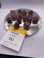 Mirror plate holding 15 strawberry quartz stones, mostly tumbled and polished, with one unpolished raw piece. A yellow lot tag labeled 'Tumbled Strawberry Quartz' is visible.