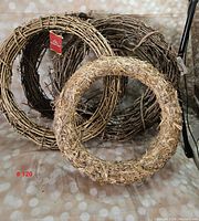 Photo showing three grapevine wreaths arranged with one wreath made of lighter, closely bound straw materials in front. Tags visible on two wreaths.