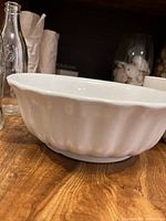 Side view of white ironstone china bowl with scalloped edges on a wooden surface.
