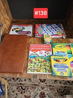 Photo showing Crayola marker and crayon boxes, three activity/coloring books, and two magazines on a wooden shelf.