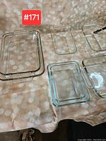 Six clear glass baking and cooking dishes of various sizes arranged on a table with a patterned cloth.