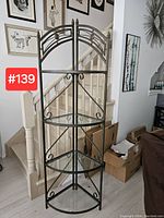 Full view of steel and glass corner shelf showing triangular corner shape and four glass shelves in steel frame.