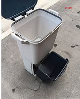 Gray plastic double compartment pet food bin with hinged lid, open showing empty interior, and small black container at base.
