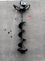 Full length view of the gas powered ice auger lying on concrete floor showing the Magnum III engine and spiral blade with handles.