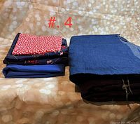 Five folded fabric materials on a patterned surface, showing different colors and types: purple corduroy, blue denim, nautical cotton with print, blue dress pants material, and silky red fabric.