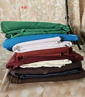Stack of nine folded fabric pieces in various colors including green, blue, white, burgundy, cream, navy, and brown, on a neutral background.