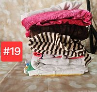 Stack of folded assorted fabrics including striped, pink textured, dark brown plush, and others