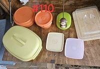 Photo showing various Tupperware items including a large yellow container with handle, orange round containers with lids, square lids, a green banana hanger with monkey, and a covered serving board.