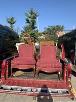 Two Louis style armchairs with red upholstery and wooden frames in the bed of a pickup truck.